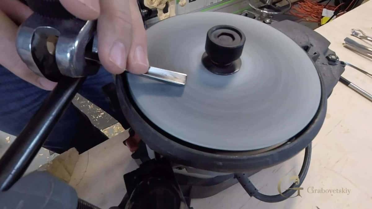 Hands guiding a V tool across the flat disc of a sharpening machine