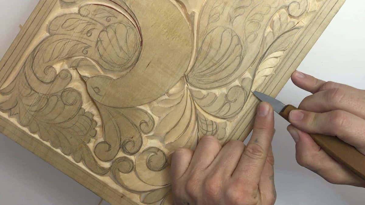 Both hands walk a small knife along a leaf edge, the whole design still pencilled underneath