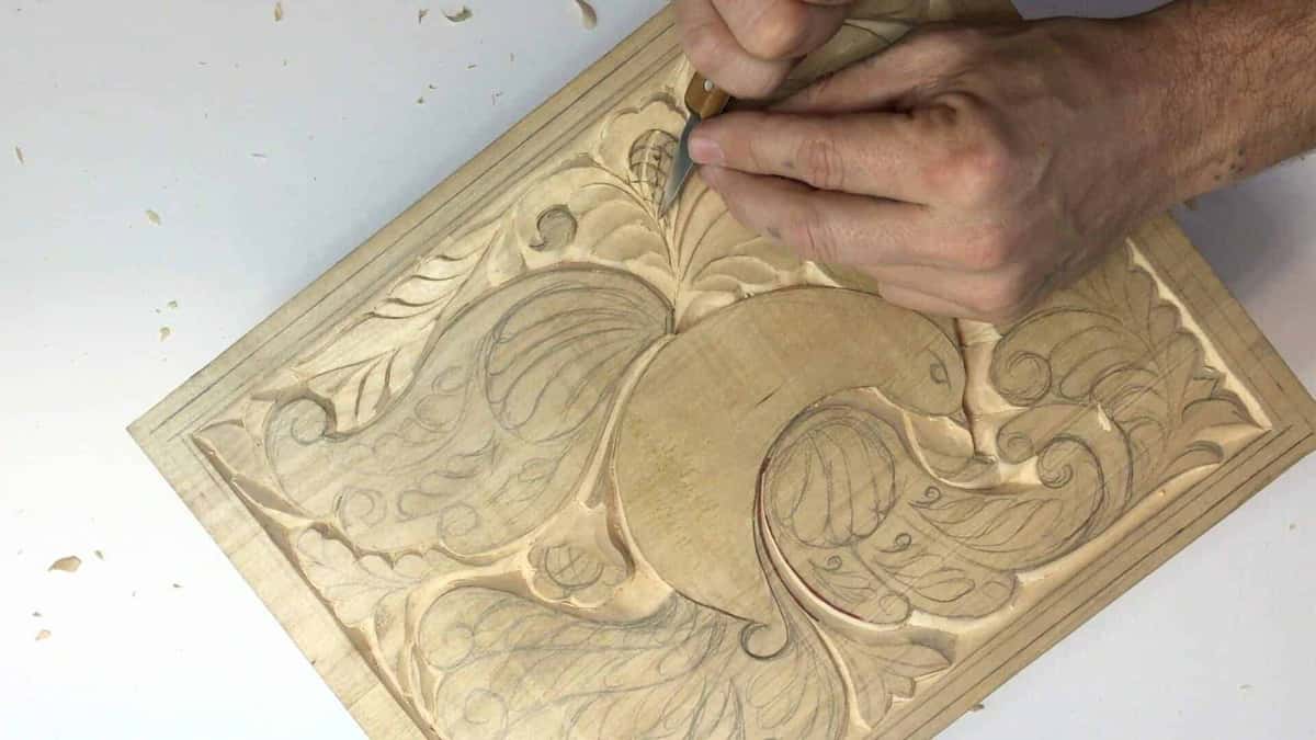 Both hands guide the knife into a bordered panel, pencil lines and chips still on it