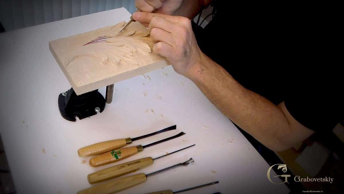 A carved panel lifted beside a row of gouges laid out on the cloth