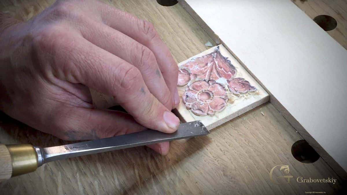 A chisel trims a small tile carved with a five petal flower