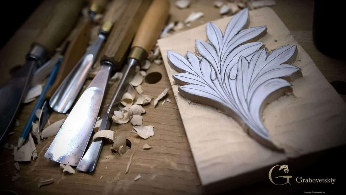 A row of gouges laid out beside a carved acanthus leaf, shavings scattered between them