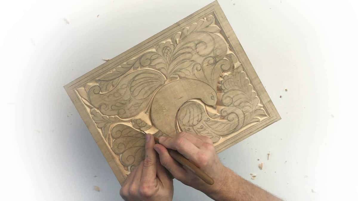 Both hands drive a gouge across the panel and shavings go everywhere on the white surface