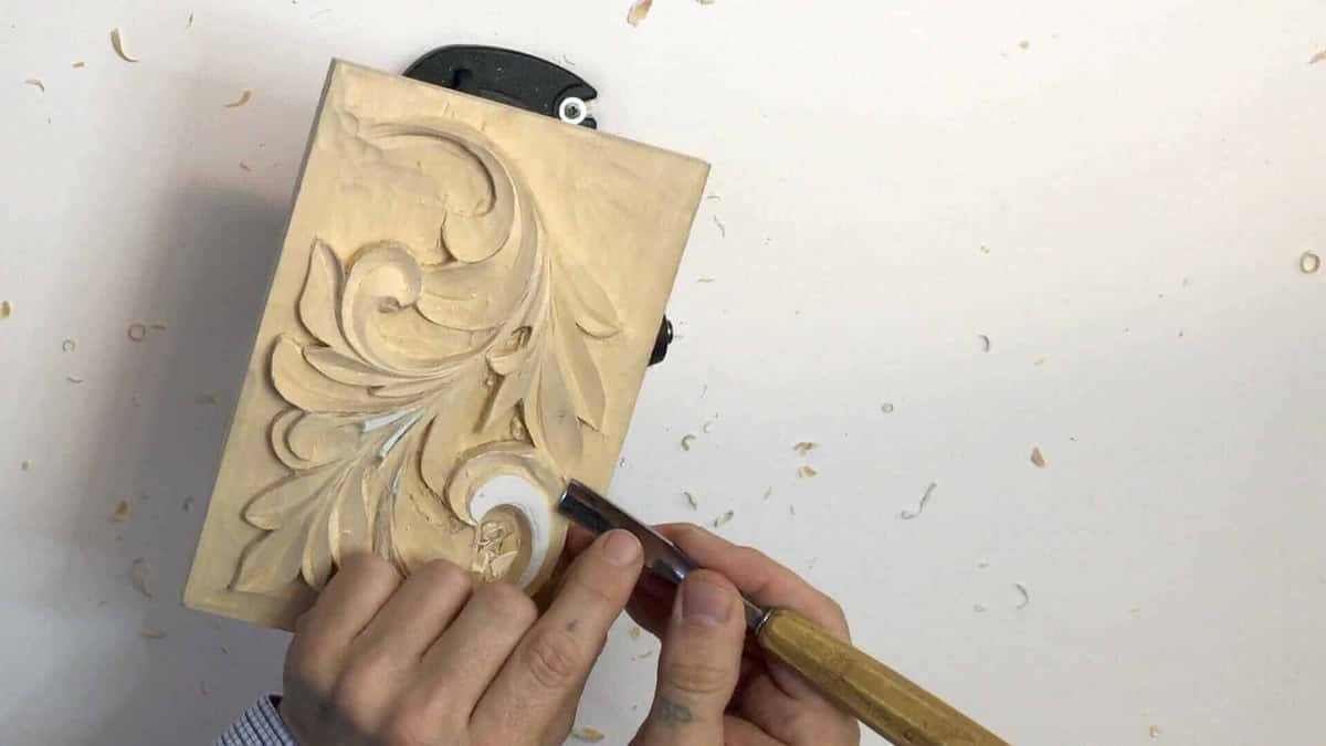 A gouge pushes through a leaf and the white table disappears under curls