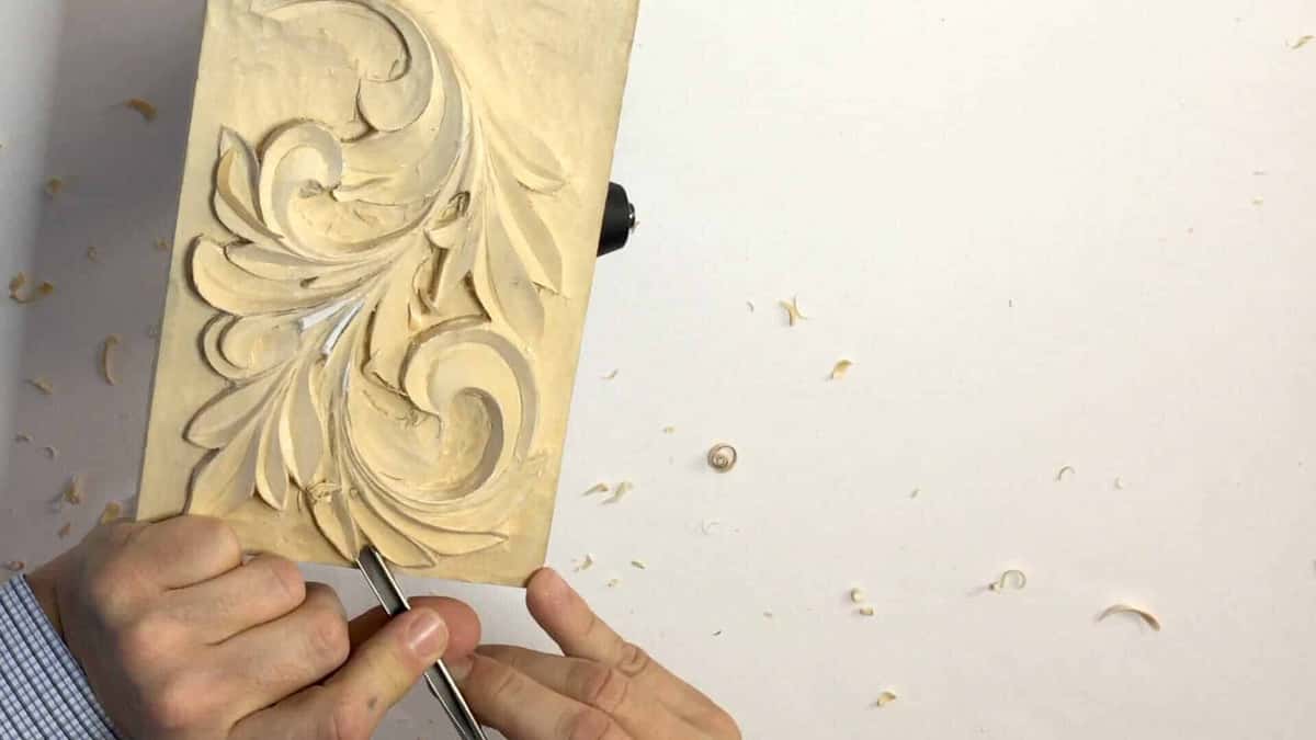 Greek acanthus scroll in pale basswood, facets crisp, shavings scattered on the white bench