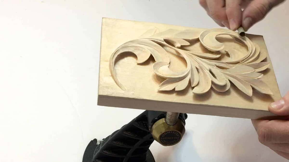 One acanthus leaf, finished, sitting on a black carver's vise while a hand checks the surface.