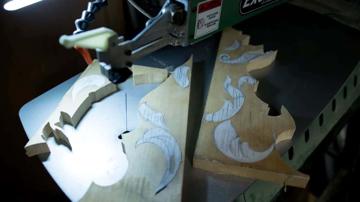 Scroll saw cutting the waste away from a carving blank, sawn parts stacked behind the blade