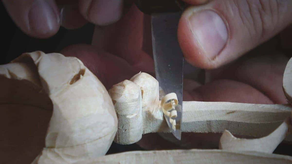Fingers and a small flat blade working behind a carved bud on a stem barely thicker than a matchstick