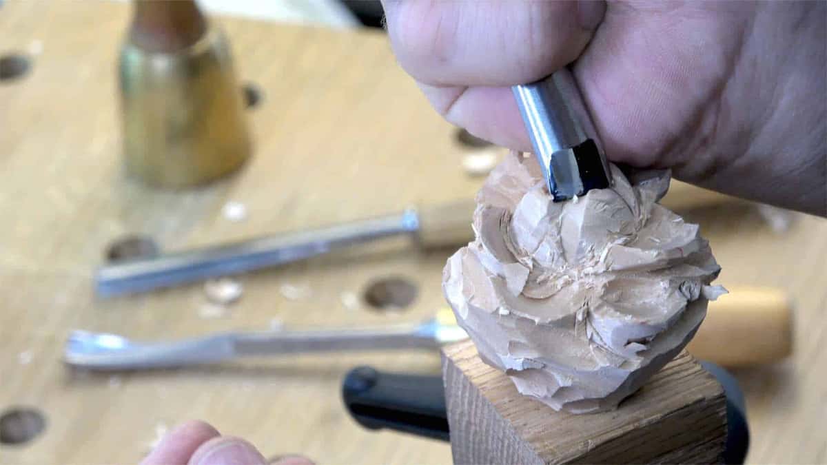 Small gouge pressed into a rough rose, brass mallet nearby.