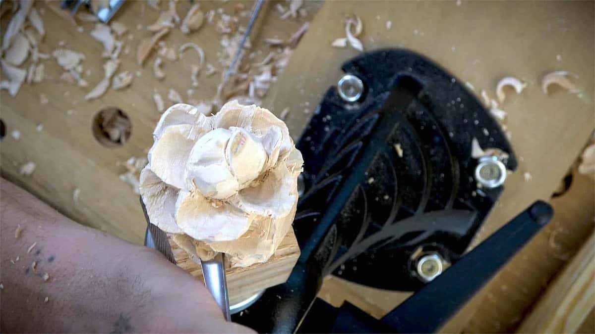 The work clamped tight inside a black carver's vise, with loose chips scattered all over the bench top.