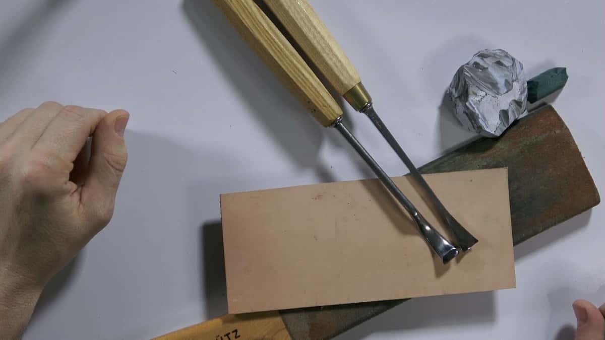 Two carving gouges resting on a leather strop beside grey and green honing compound