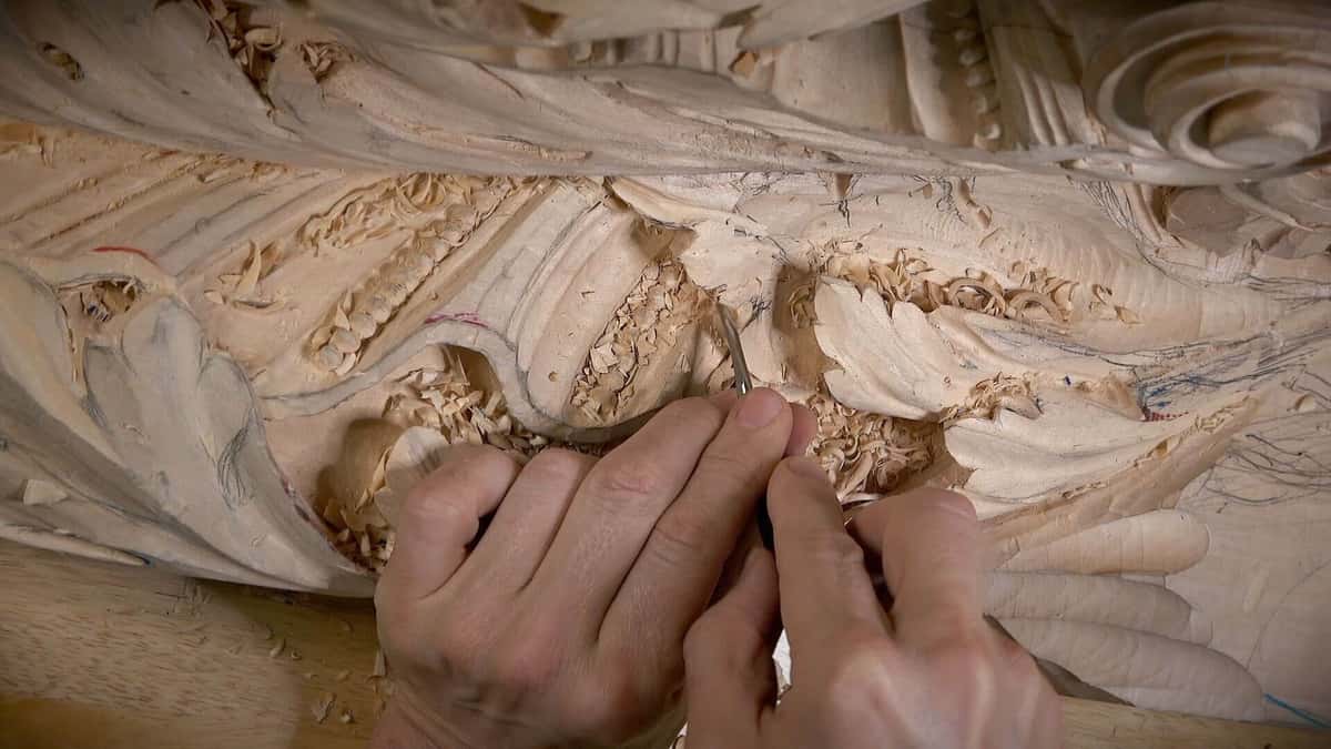 Hands with a small tool in a dense relief covered in chips, pencil layout lines still visible.