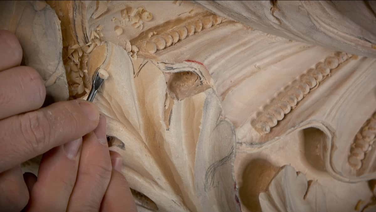 Loose pale curls beside a slim tool working the junction of two carved lobes