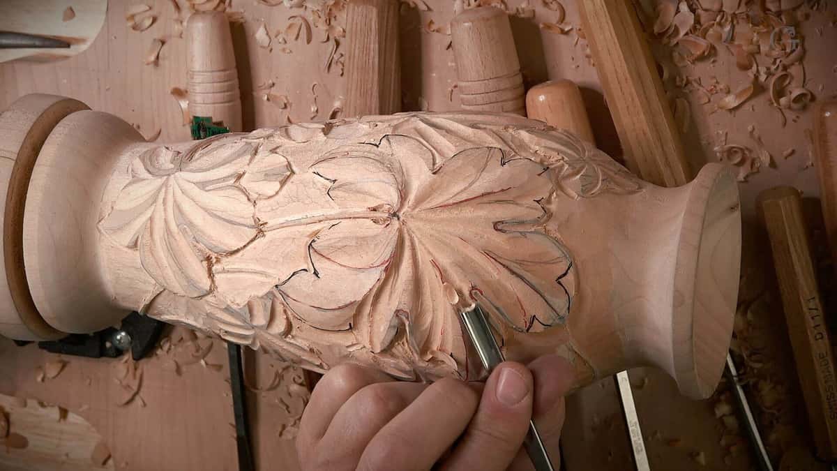 Smooth turned neck beside tool carved grape leaves, all bare wood.