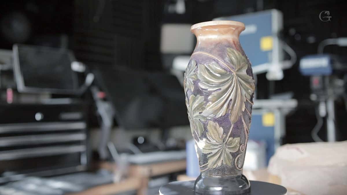 Finished carved vase with green grape leaves over a purple ground, glossy under shop lights.