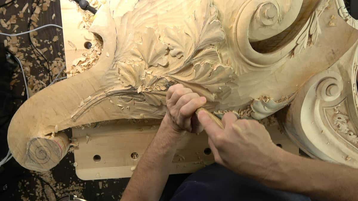Big carved pediment on the bench, acanthus and volutes roughed out in pale wood.