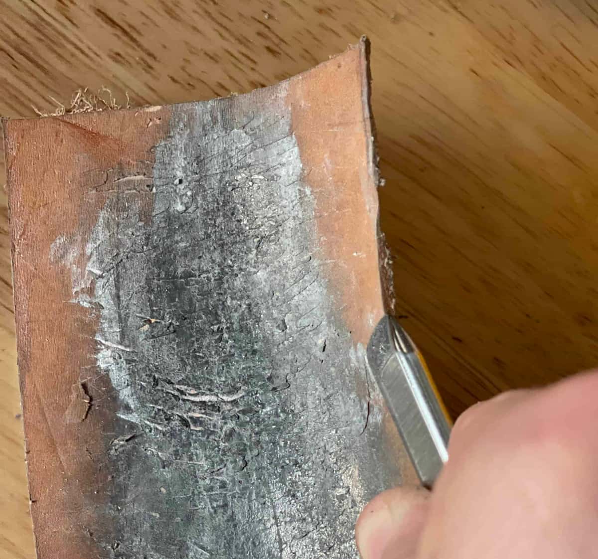 A V tool pulled backwards along a bare leather strop lying on the benchtop