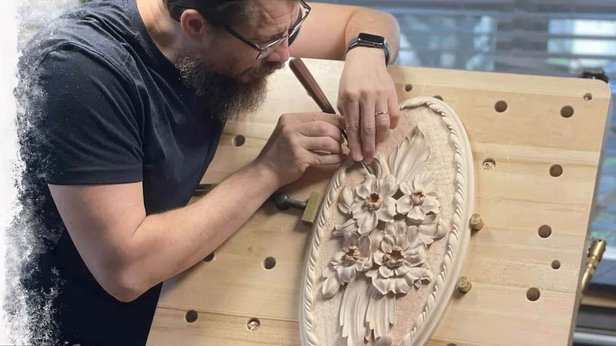 Alexander leans over the bench, working small detail into an oval flower rosette