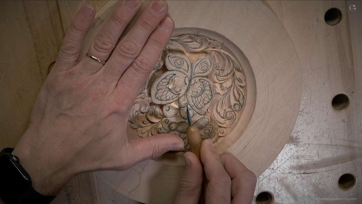 A close-up view of a person's hands carving a detailed butterfly design into a wooden plate, showcasing intricate patterns. Learning this skill raises the question: how long does it take to learn how to carve wood?