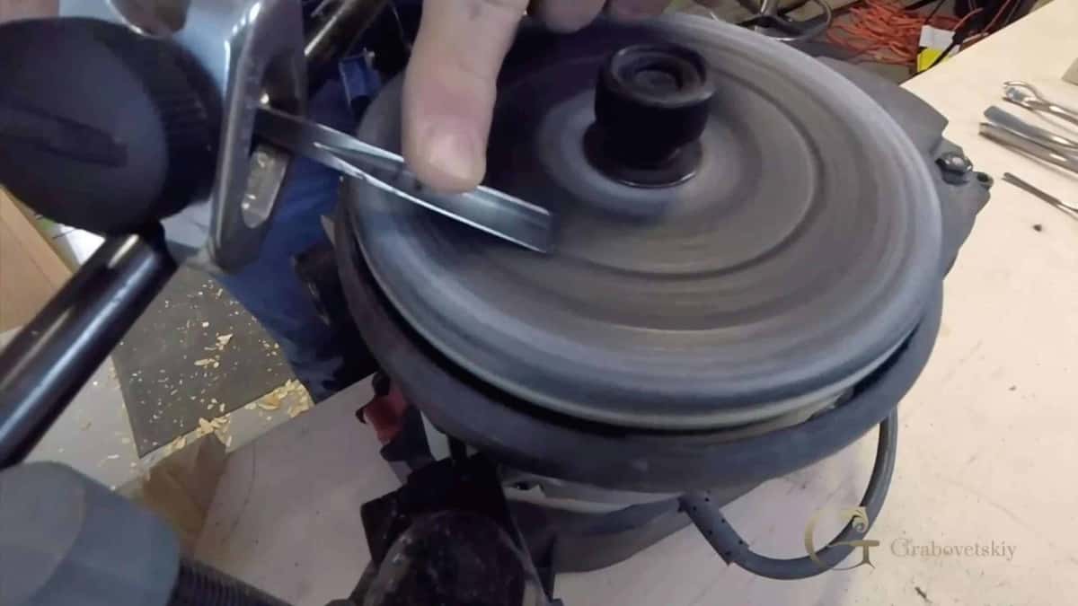 A gouge held against a spinning honing wheel, with chips and workshop clutter behind