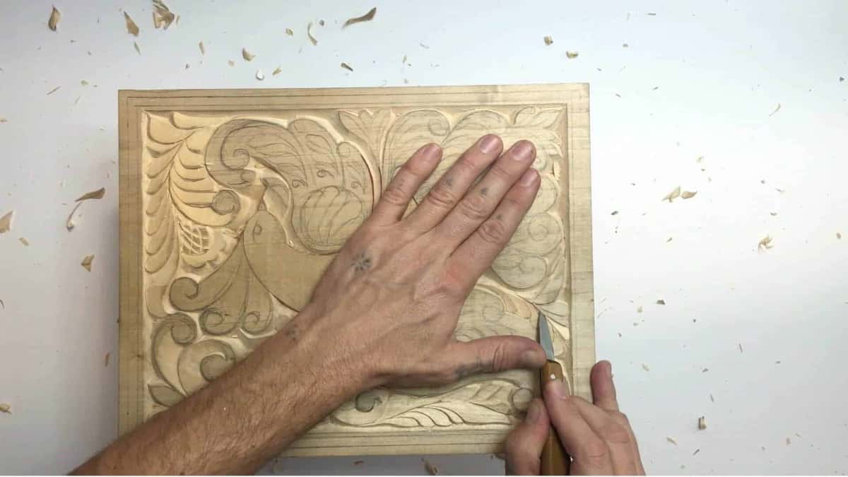 The left hand lies open and flat on the carved board while the right works a small knife at the edge