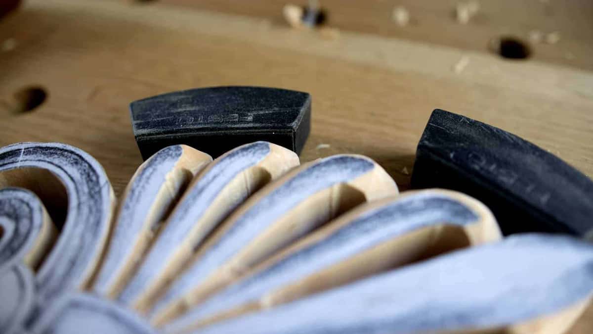 Close view of carved petal ridges darkened with graphite, two black sanding blocks parked on the bench behind
