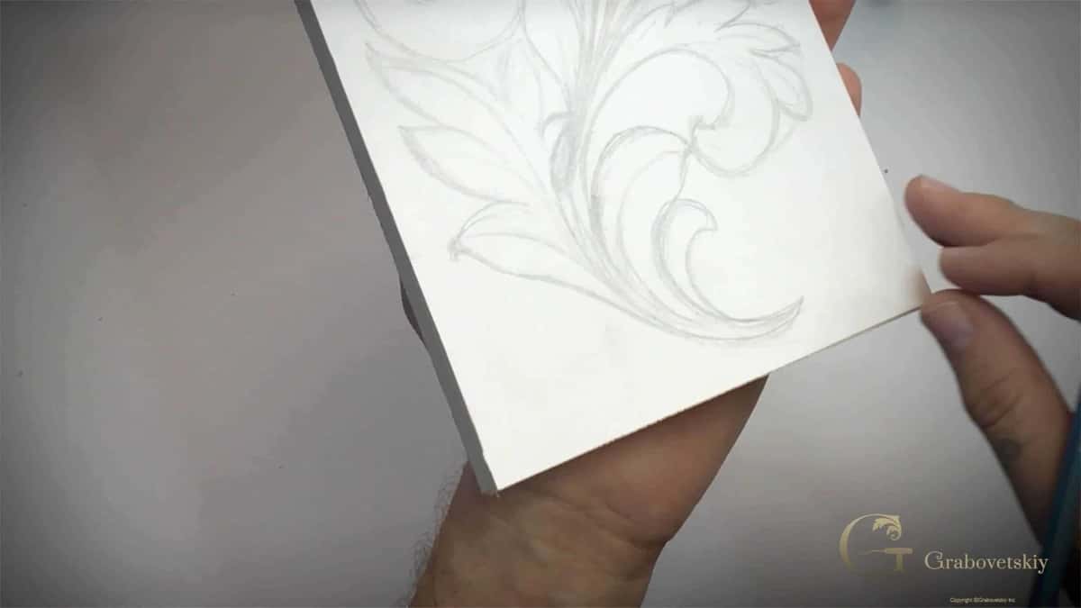 A hand holding a board with the whole Greek acanthus leaf drawn on it in pencil, ready to cut
