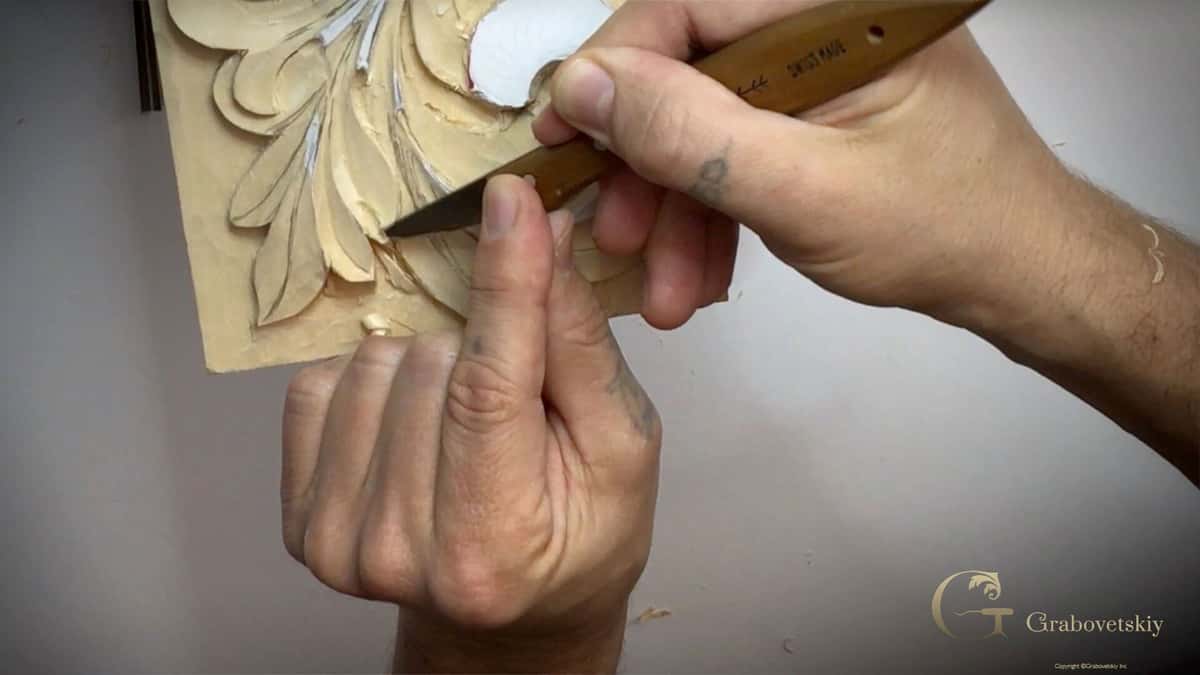 Skew pointed Swiss blade steadied by a thumb, taking one pass in the corner of an acanthus study