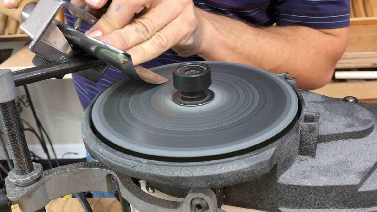 A large gouge clamped in a jig arm and held against the spinning sharpening disc