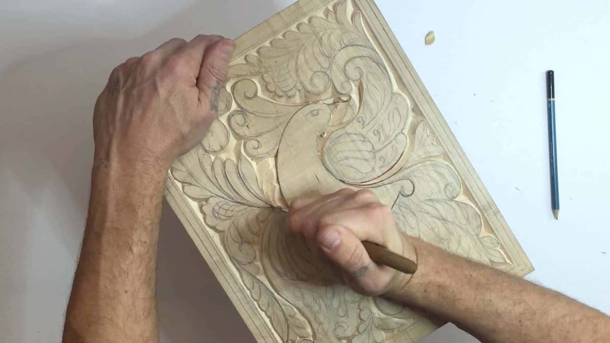 Pencil laid beside a part carved bird panel on a bare white bench top