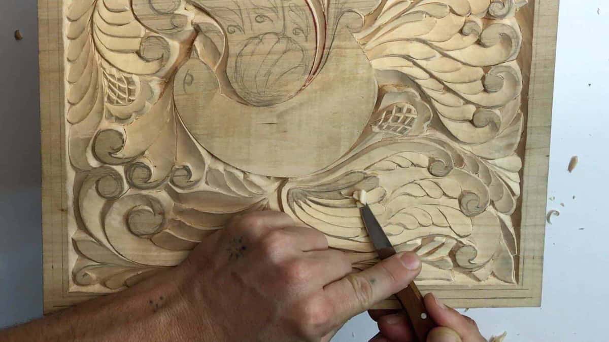 One hand drives a brown handled knife through a leaf on the carved board, pencil lines still showing beside it