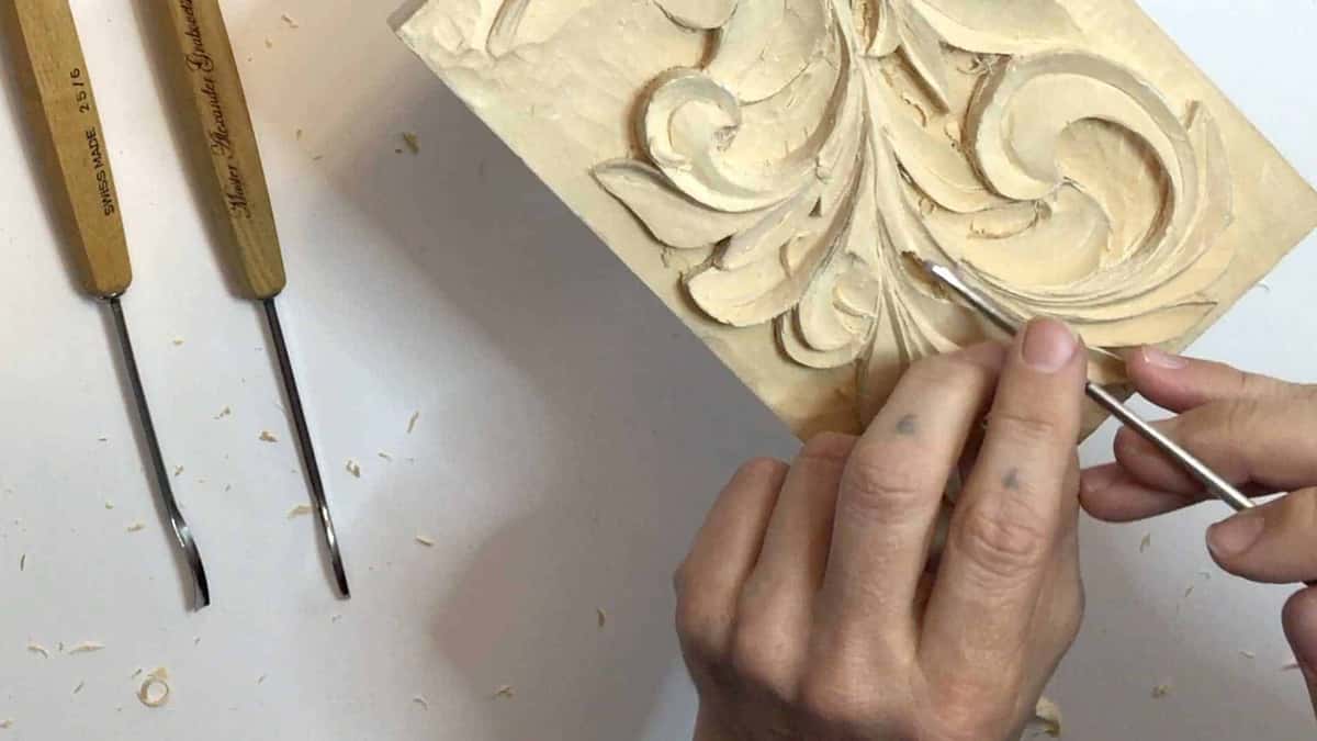 Only three tools in sight, two long shanked spoon gouges on white and one cutting the acanthus block
