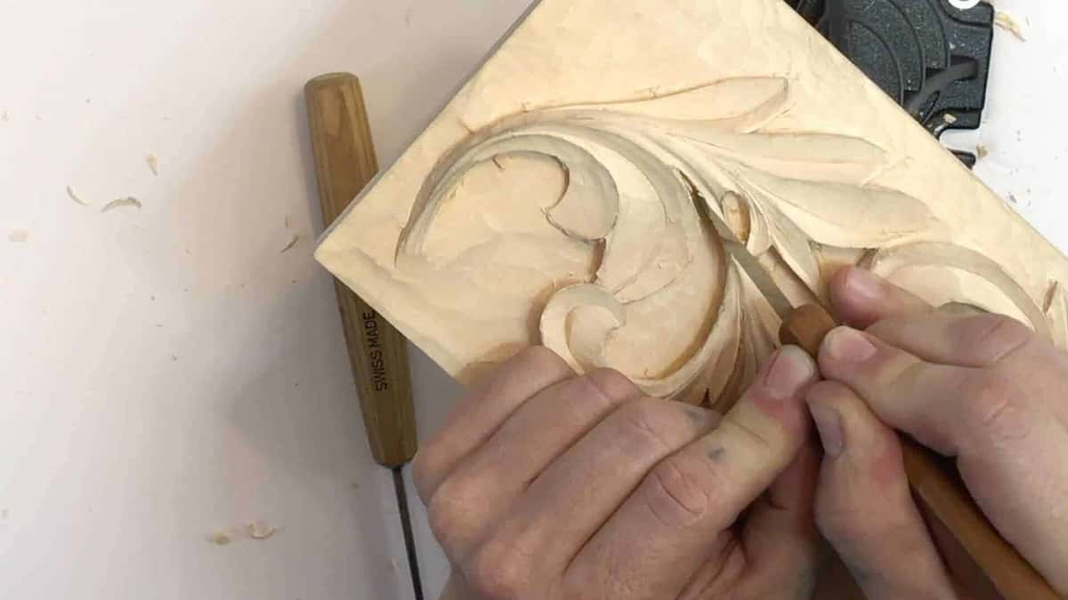 Slim Swiss stamped tool waits on white beside a carved acanthus block