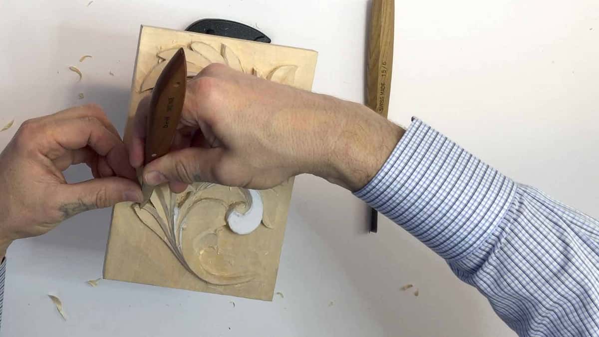 A small unclamped panel held in the left hand while a long carving knife works the leaf below