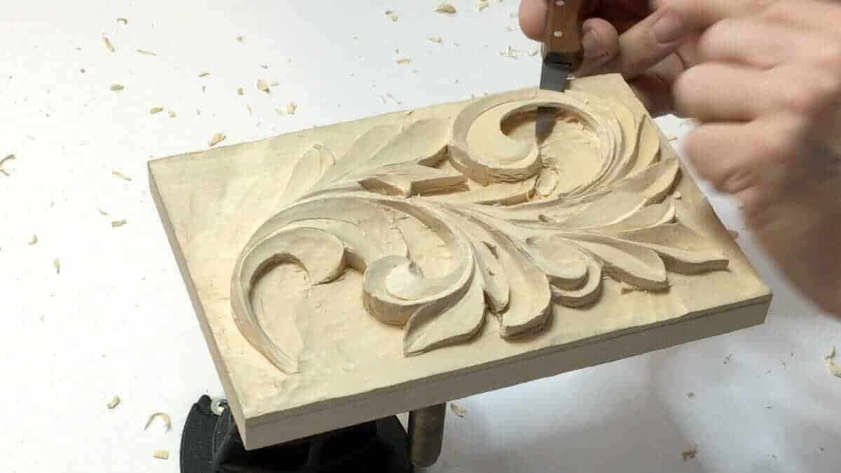 A finished acanthus panel still clamped on the bench with chips scattered around it, the shape a practice board can reach