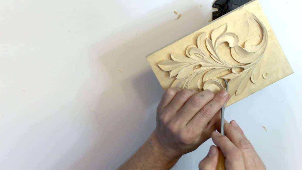 Both hands holding a small pale acanthus panel, the kind of soft practice board a new carver should start on