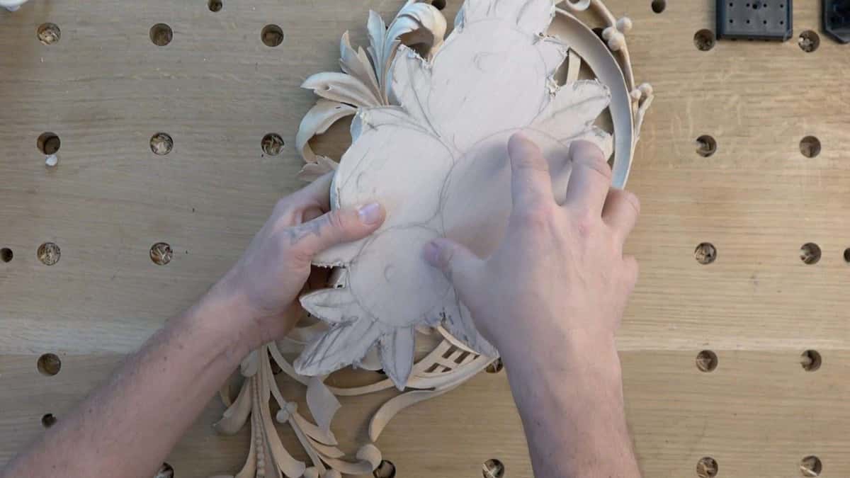 Both hands cradling a pierced acanthus rosette, fingers taking its weight from underneath