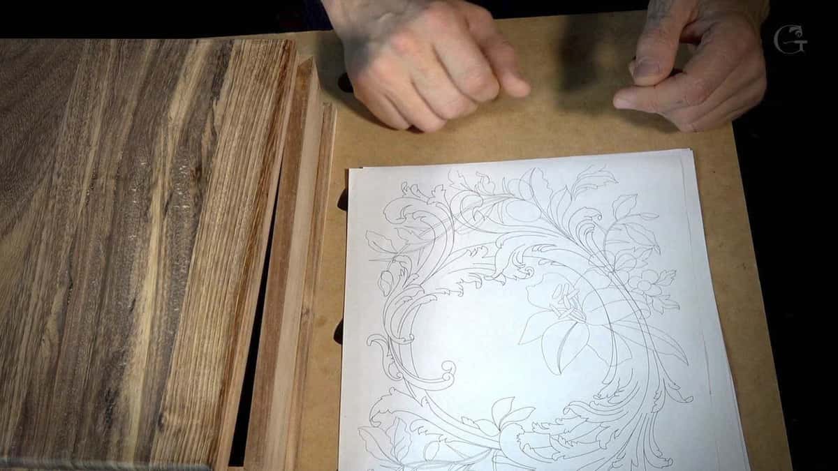 Brown streaked board rests beside a paper drawing of the wreath that will be carved into it