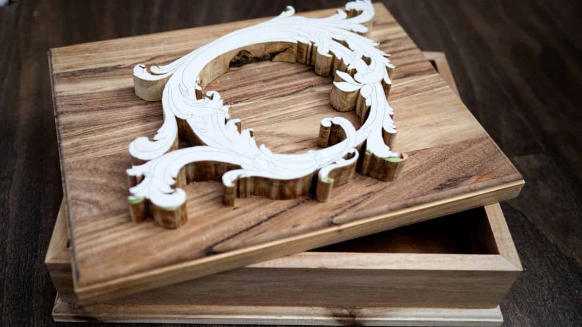 Pattern cut-out resting on a bare acacia lid, showing where the carved wreath will sit