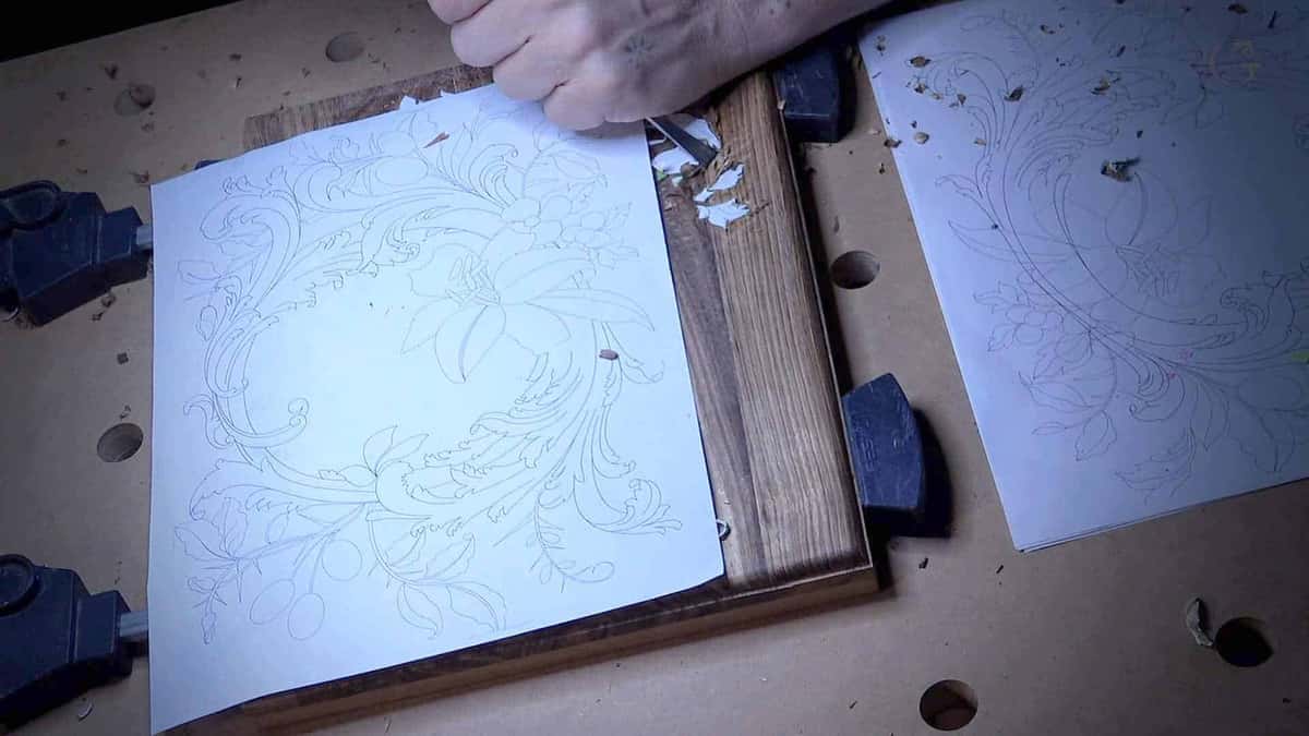 Paper pattern sheet laid over a dark board clamped for carving