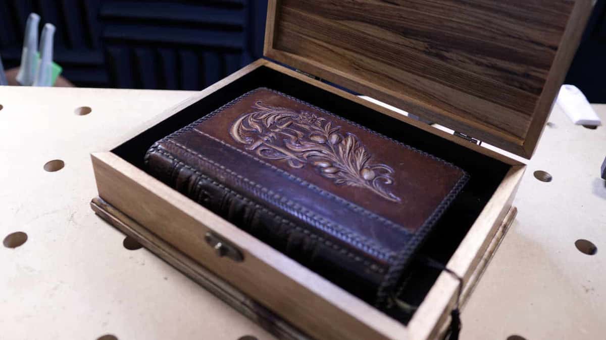Open box lid raised on its hinges with a tooled leather book resting inside, plain surfaces within