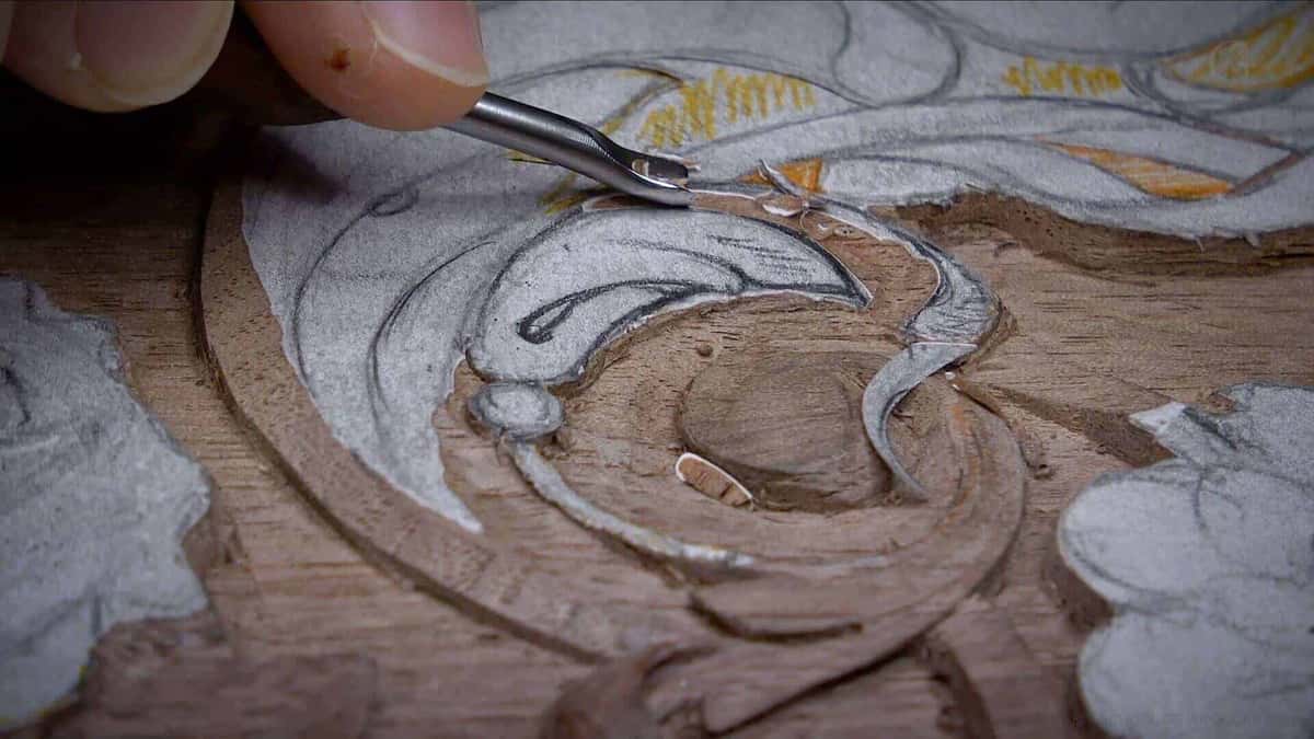 Outlining a drawn scroll with a small gouge, the grey paper pattern still stuck over the wood just beneath
