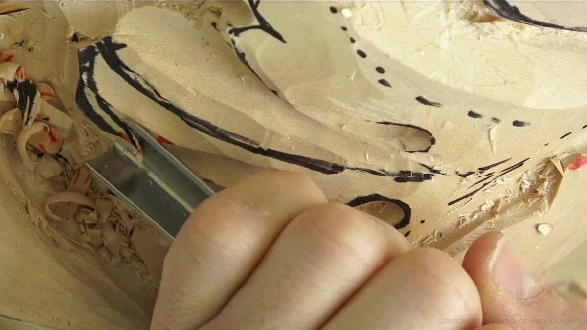 Small chisel set against a heavy marker line on a roughed basswood leaf, chips lying at the left