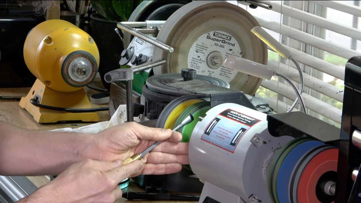 Bare hands holding a gouge against a stack of colored buffing wheels