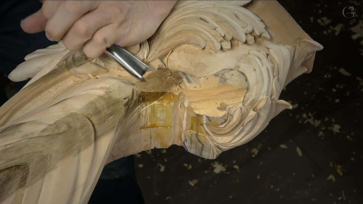 Closed fist driving a wide gouge into deep acanthus