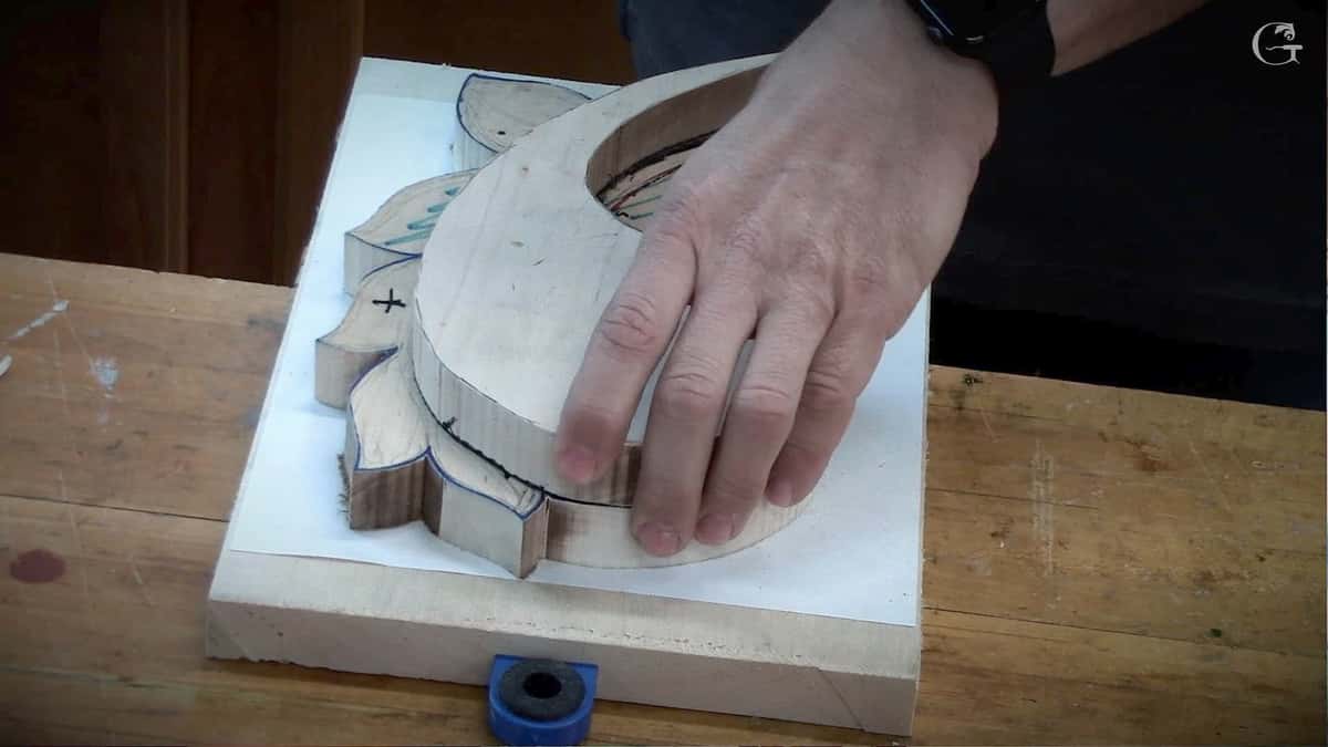 Sawn waste blocks lifting away from a roughed acanthus blank, hands steadying the piece on the bench top