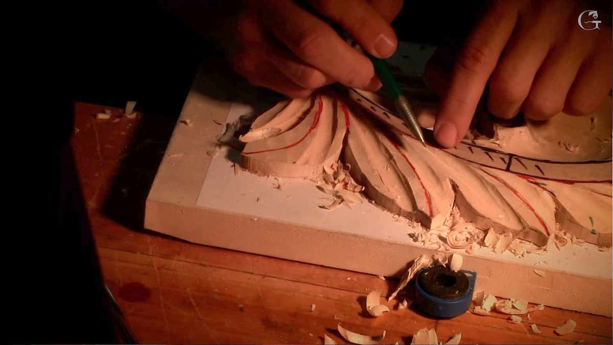 Two hands steadying a Byzantine acanthus leaf while a fine pointed tool scores a line through the chips