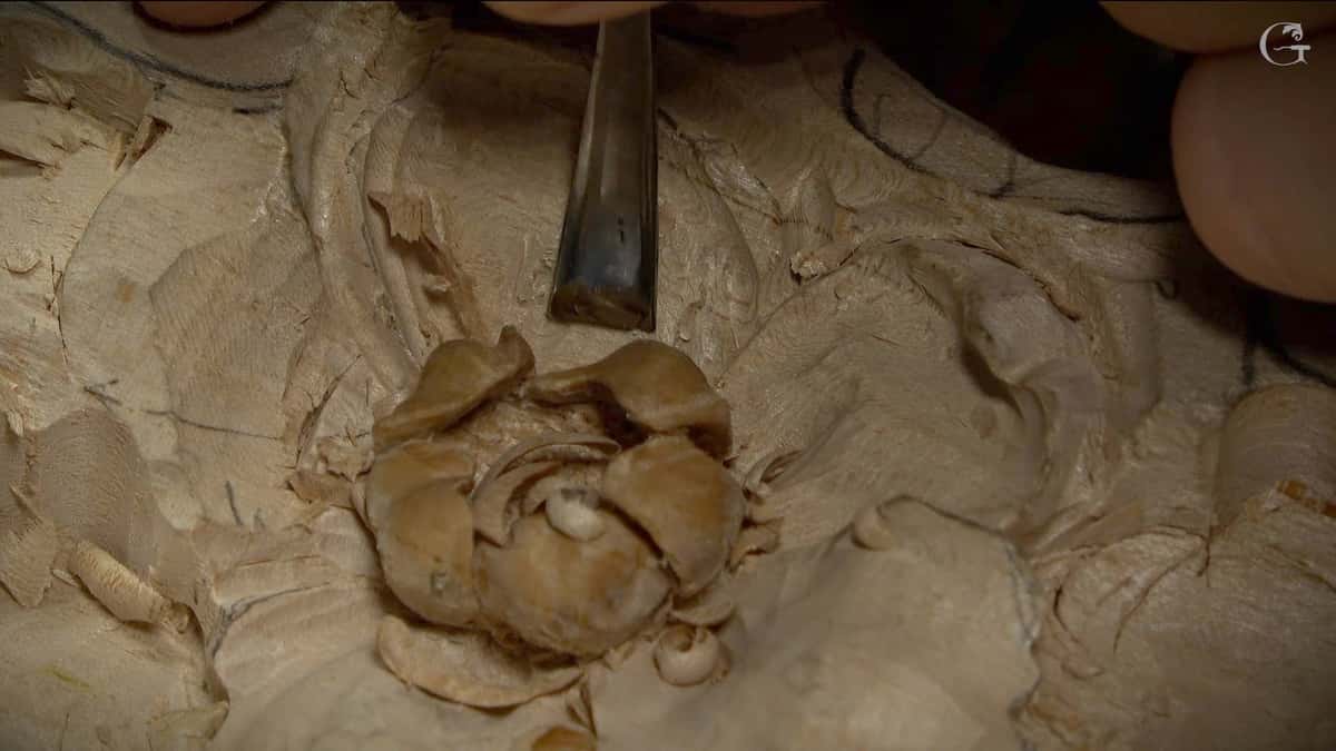 Narrow gouge held over a small carved rose whose petals overlap into deep shadowed pockets