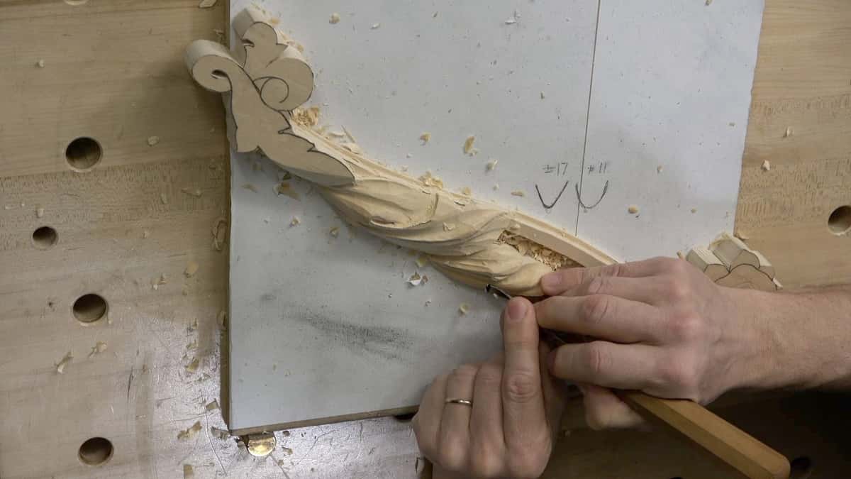 Bench dog holes, shavings, and a hand pinning a slender acanthus molding