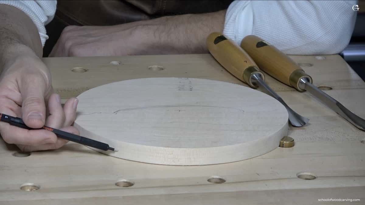 Round basswood blank marked in pencil beside two carving gouges